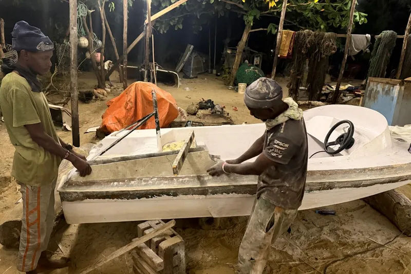 Two young men building a fibreglass boat at night