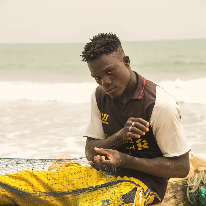 A young man mending nets on the beach